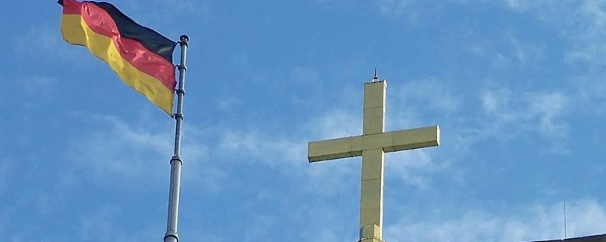 Das vergoldete Kreuz auf dem Bergfried der Wartburg sowie die Fahne der Bundesrepublik Deutschland (Wikipedia)